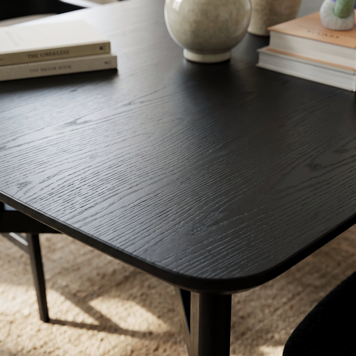 Modern dining room with a sleek black wooden table, minimalist decor, and a textured rug in a contemporary home.