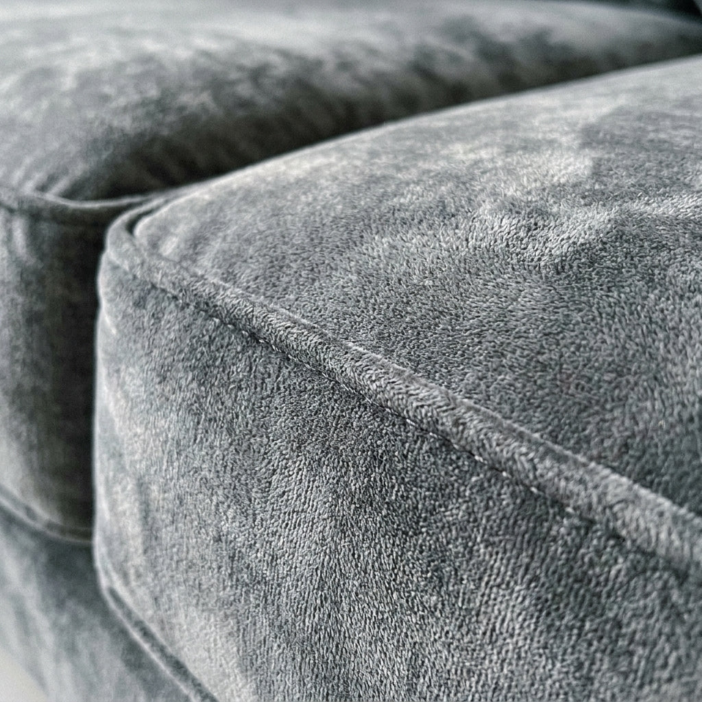 Close-up of a modern grey velvet sofa cushion with detailed piping, showcasing soft, plush fabric texture.