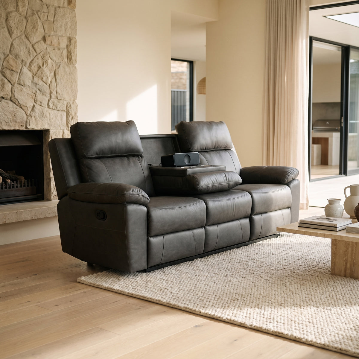 Tiberius reclining sofa in charcoal grey beside a stone fireplace, on a chunky wool rug over pale oak boards