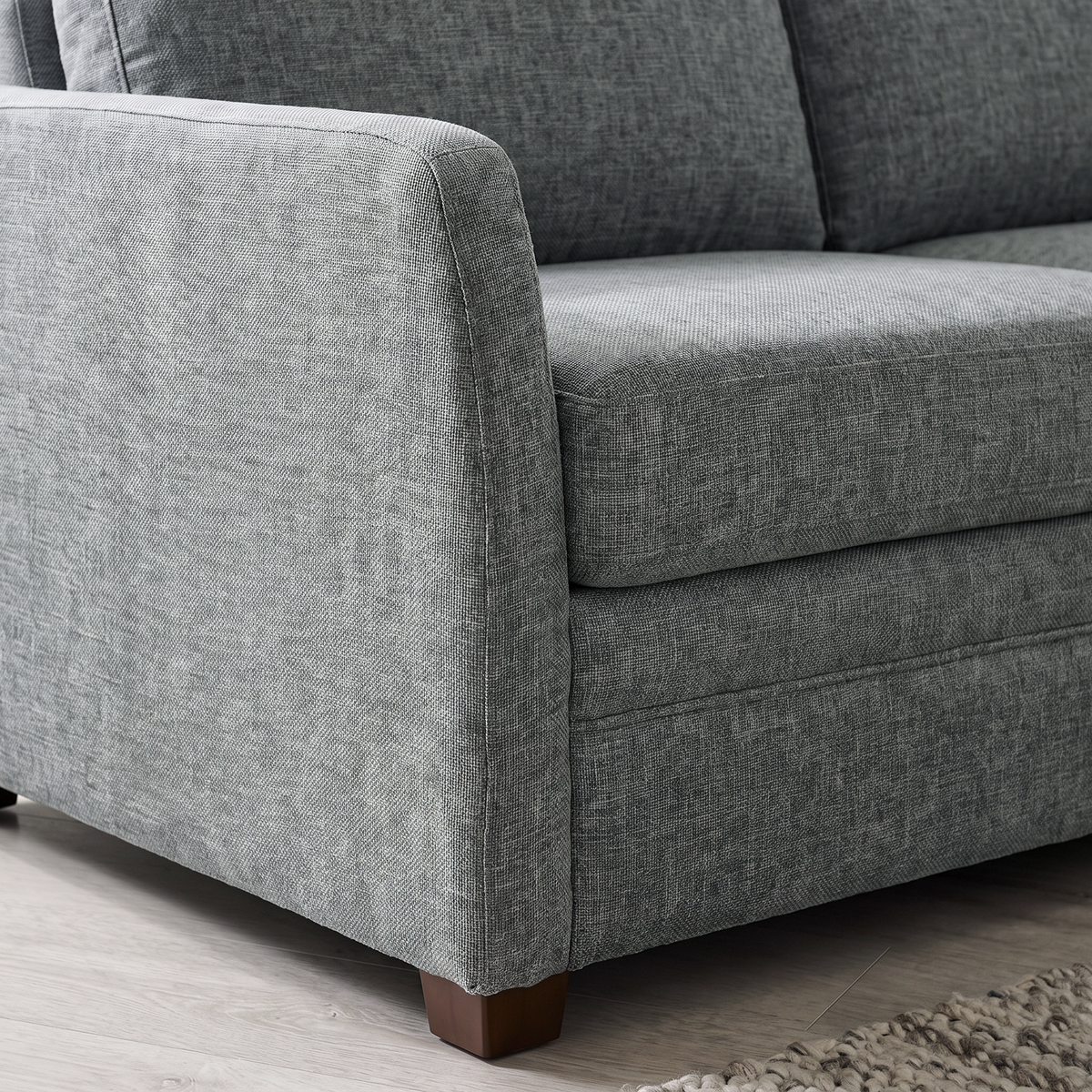 Close up of the track arm, grey woven fabric and dark wooden block foot on the Kane sofa bed