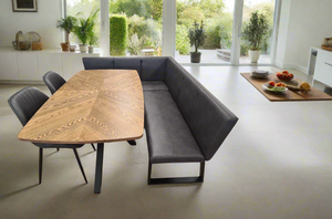 Modern dining set with a corner bench and two chairs, featuring a medium oak table top and metal legs, set in a bright room with plants and a window view.