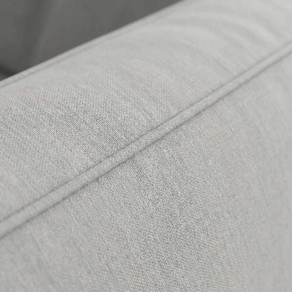 Close-up of a modern light gray fabric sofa featuring clean lines and elegant piping detail for a minimalist living room.