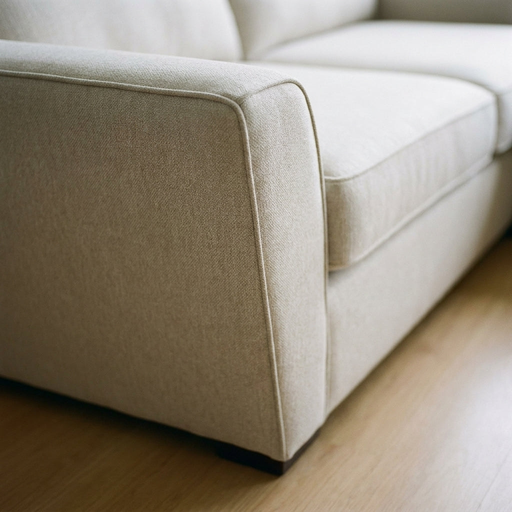 Close-up of a modern beige fabric sofa with clean lines, placed on light wood flooring in a minimalist living room.