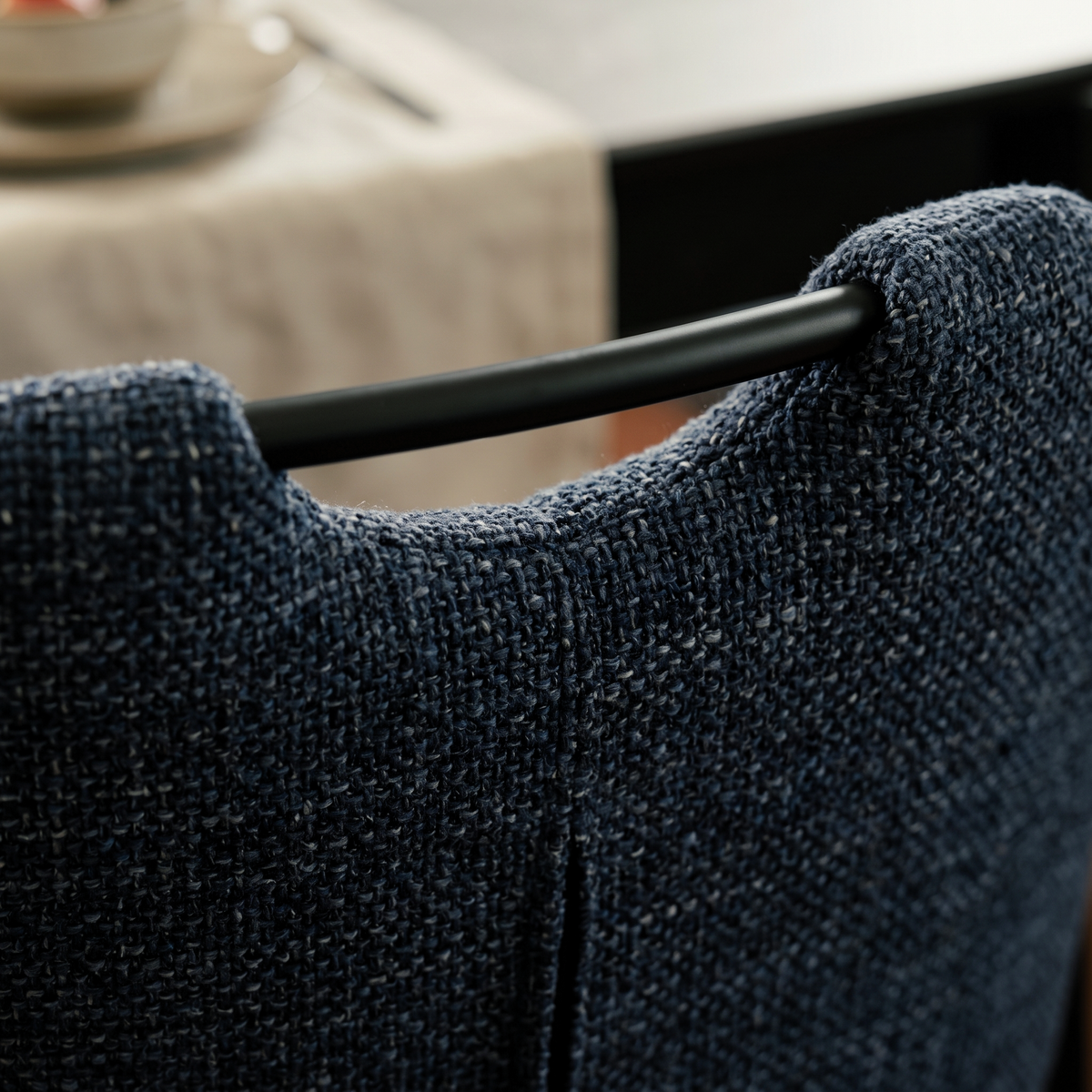 Close up of a Mischa dining chair showing the black metal grab handle set into the navy flecked tweed backrest