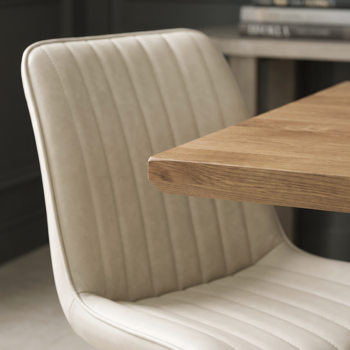 Close up of a Sloan dining chair showing the vertical channel stitching in cream faux leather beside the chamfered oak edge of the table top