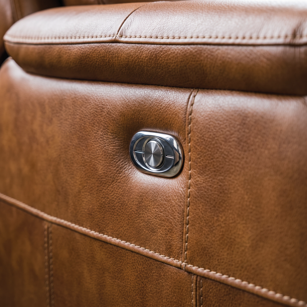Close up of the chrome recline control button and tan leather grain on the Sterling electric recliner
