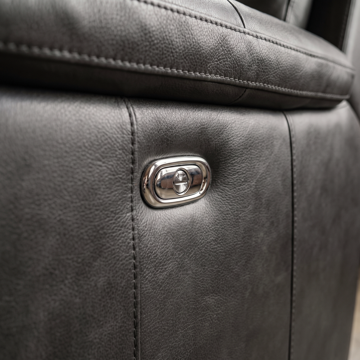 Close up of the chrome recline control button and charcoal leather grain on the Julius recliner
