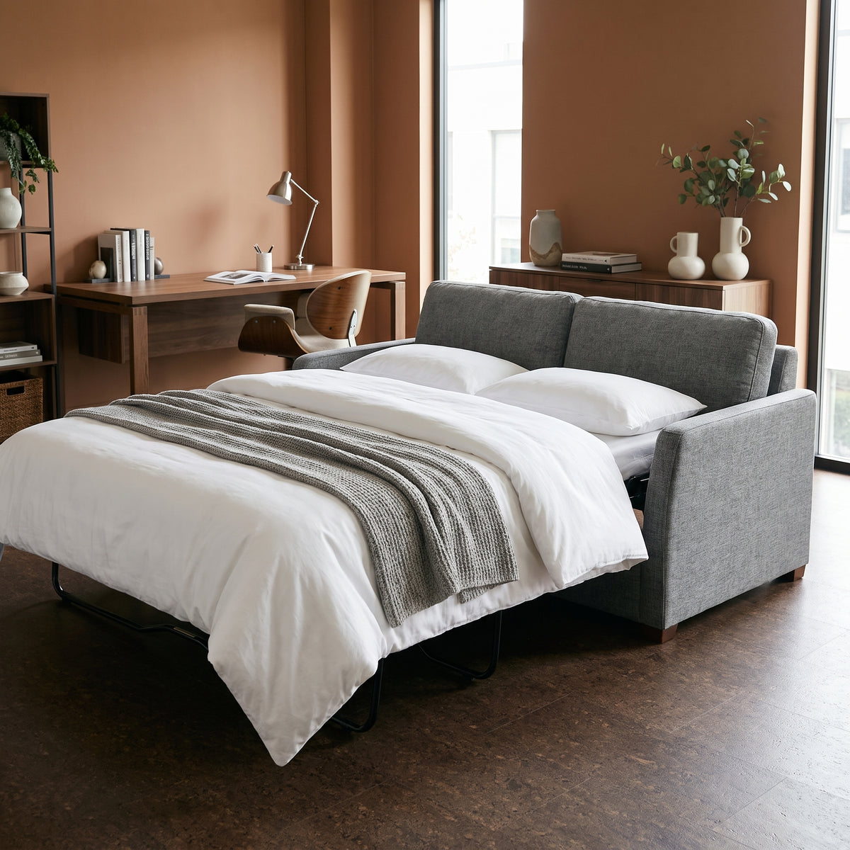 Kane sofa bed with the bed pulled out and made up, in a spare room with warm clay walls and a desk