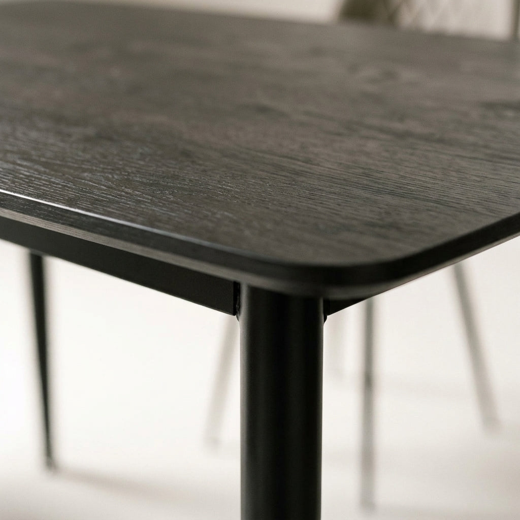 Close up of the Casey dining table corner showing the dark charcoal woodgrain top and slim black tapered leg